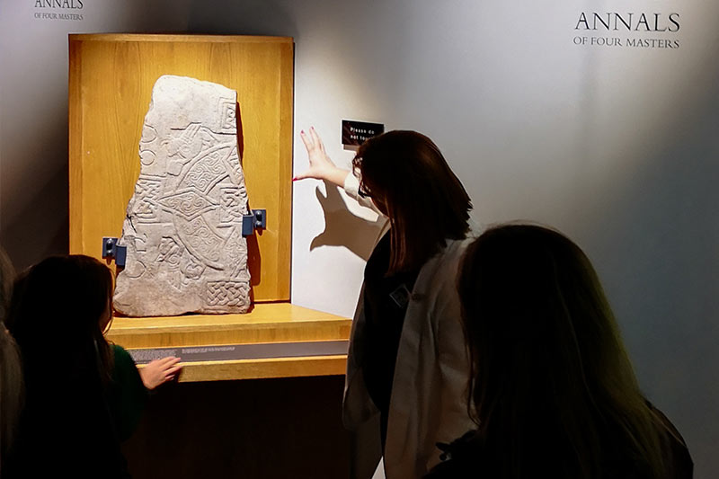 Athlone Castle tour guide presenting one of the stone slabs from early Christian times on display in the Early Settlement exhibition at Athlone Castle Visitor Centre.
