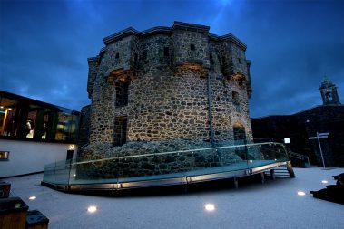 The Athlone Castle Keep stands strong in the centre of the castle courtyard lit up at night and surrounded by dark navy blue skies.