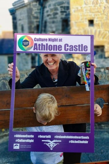 Taking advantage of a great photo opportunity woman is holding Insta frame in front of a boy locked in the medieval castle stocks during Culture Night at Athlone Castle.