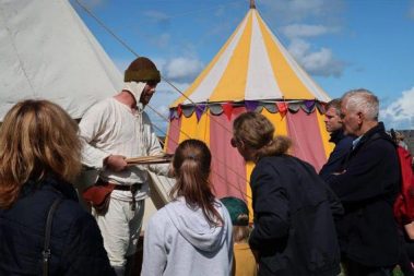 Bow maker Jack demonstrates how medieval bows and arrows were made. Onlookers listen carefully as he explains the skills that are required to become a master bow maker.
