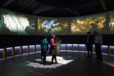A group of people experiencing the Siege 360 exhibition at Athlone Castle Visitor Centre. Surrounded by projections of images and re-enactments from the Great Siege of Athlone in 1691.