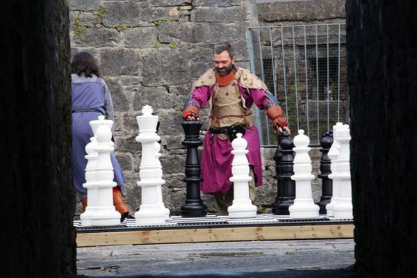 A man dressed in medieval clothing playing giant chess