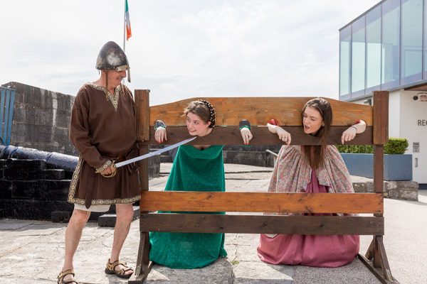 Three visitors dress up in medieval costumes are having fun with replica stocks at Athlone Castle Visitor Centre